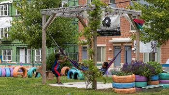 Two kids play in a colorful hammock in a park.
