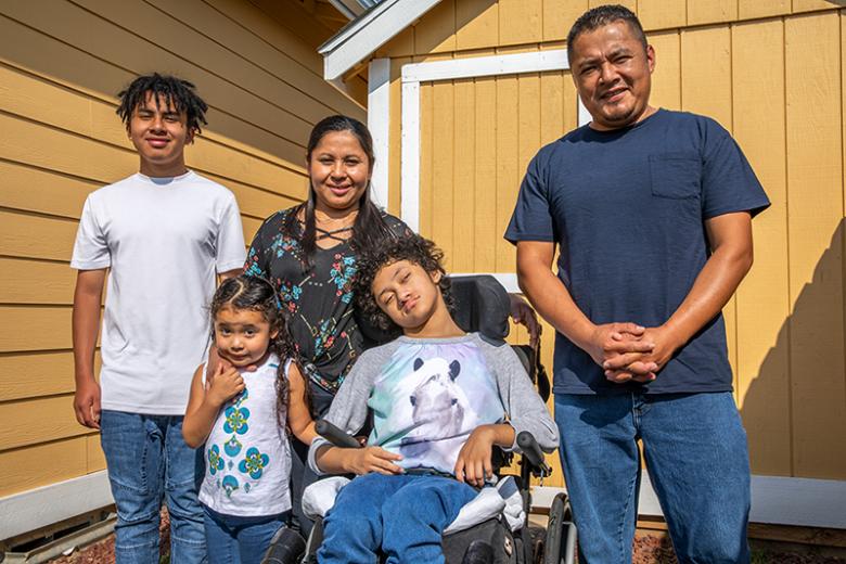 Parents with three kids, including one child in a wheelchair, in front of their home.