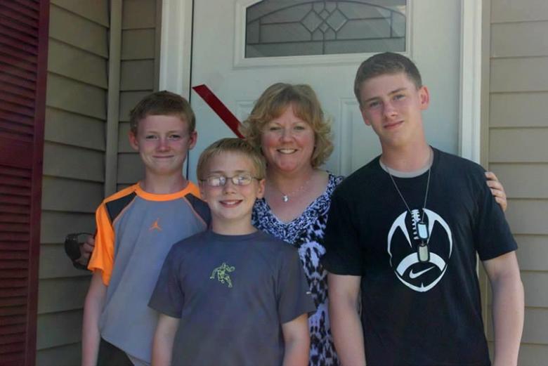 Amy with her three sons posing and smiling by their front door.